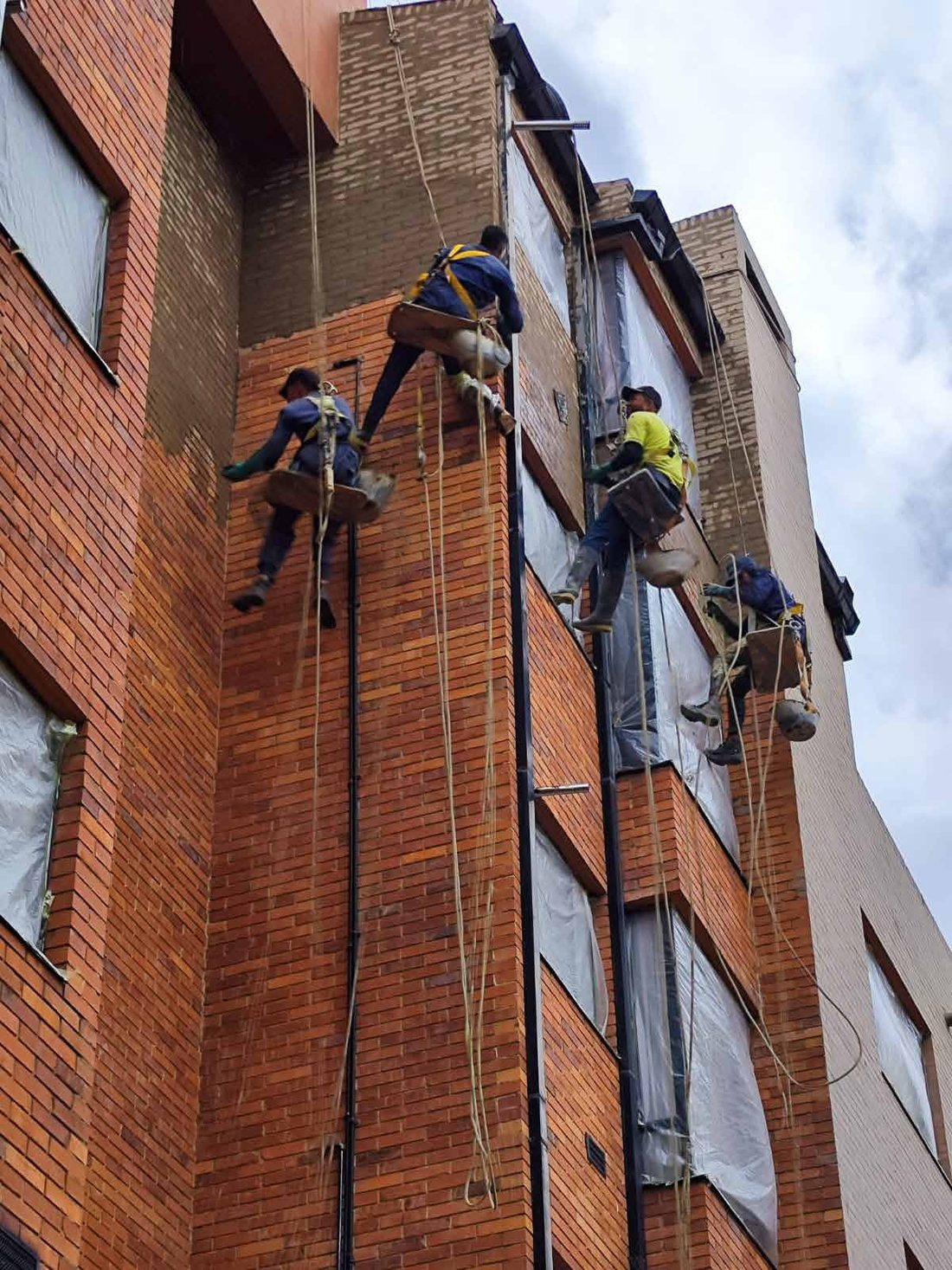 Cuatro operarios descolgados con cuerdas trabajando simultáneamente sobre la fachada de un edificio