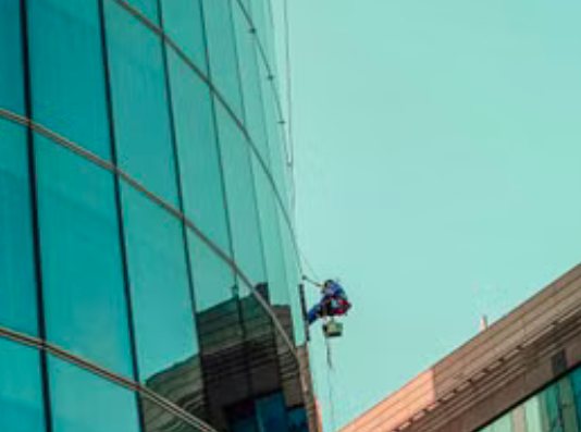 Operario descolgado sobre la fachada acristalada curva de una torre corporativa