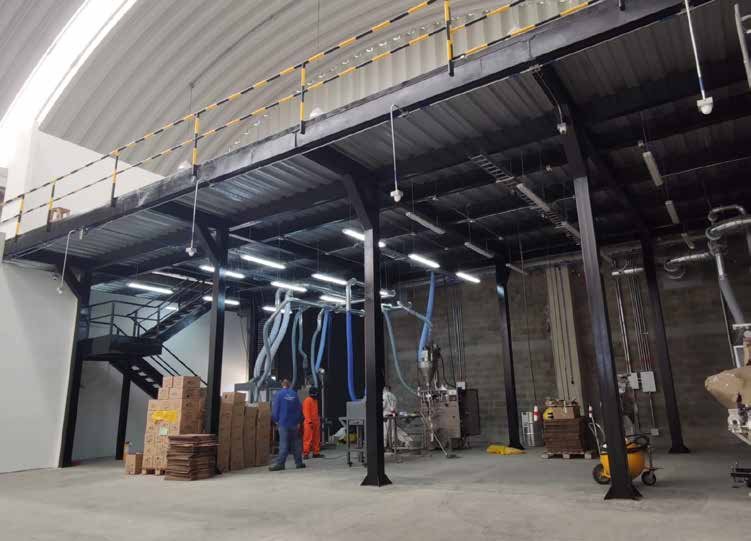 Interior de bodega en obra con estructura metálica, mezanine y personal trabajando